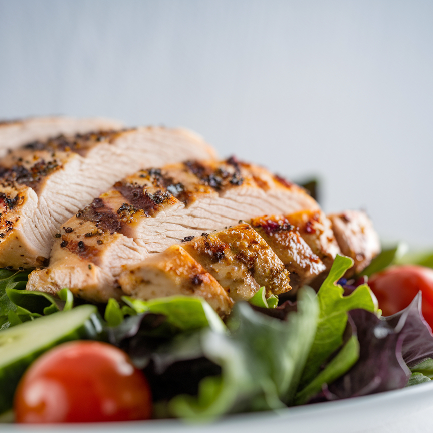 A vibrant grilled chicken salad with mixed greens, cherry tomatoes, and avocado slices.